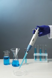 Laboratory analysis. Scientist dripping sample with micropipette into petri dish at white wooden table, closeup