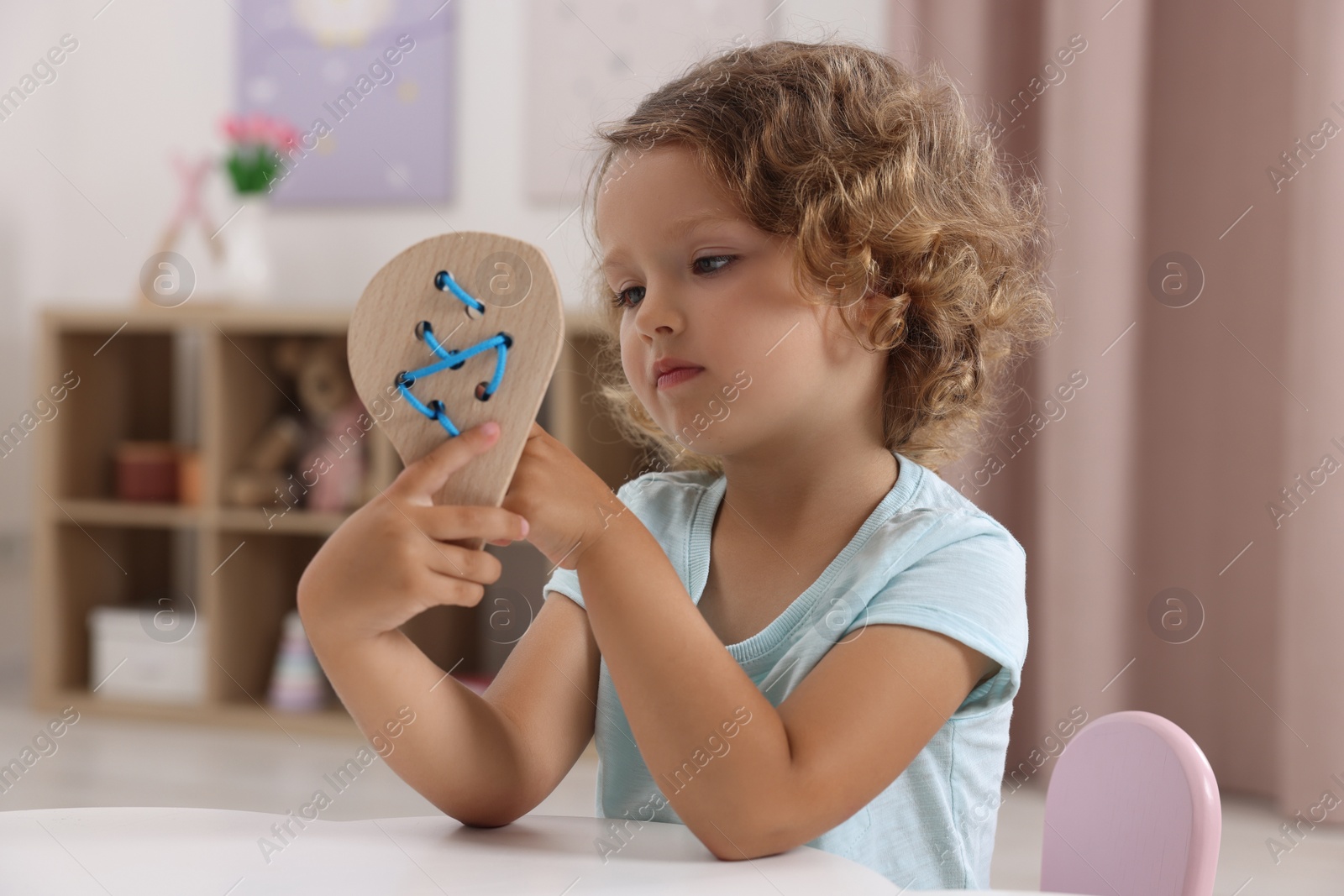 Photo of Motor skills development. Little girl playing with wooden lacing toy at table indoors