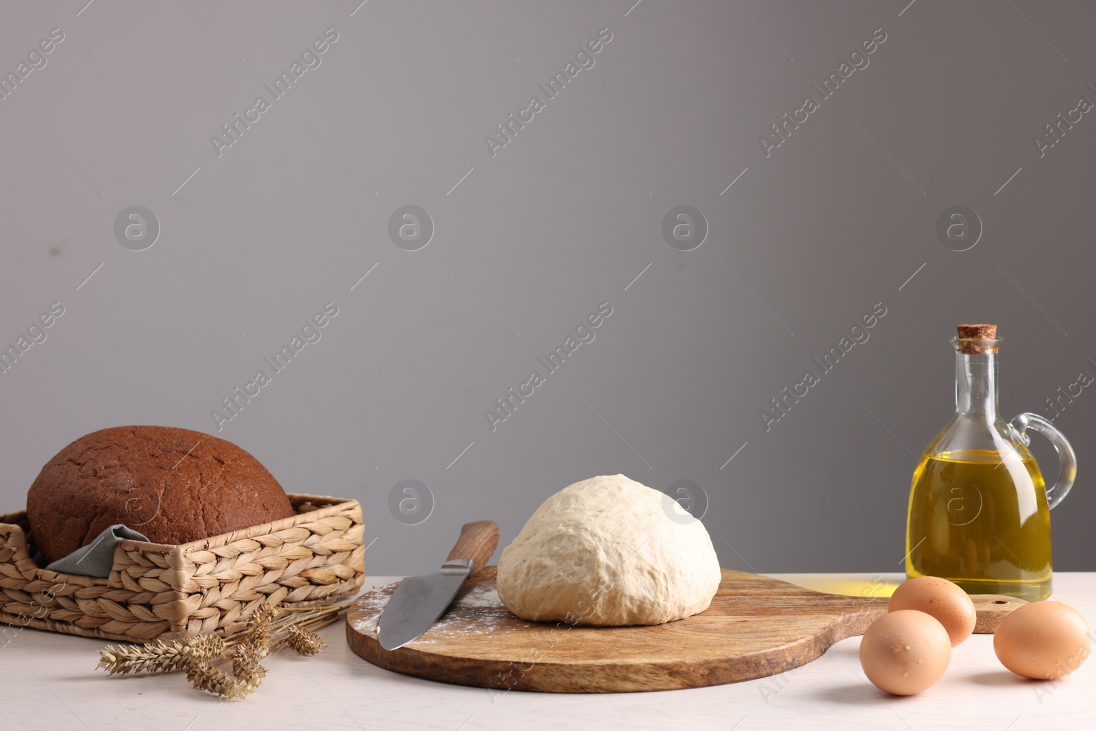 Photo of Fresh dough sprinkled with flour and other ingredients on white table near grey wall