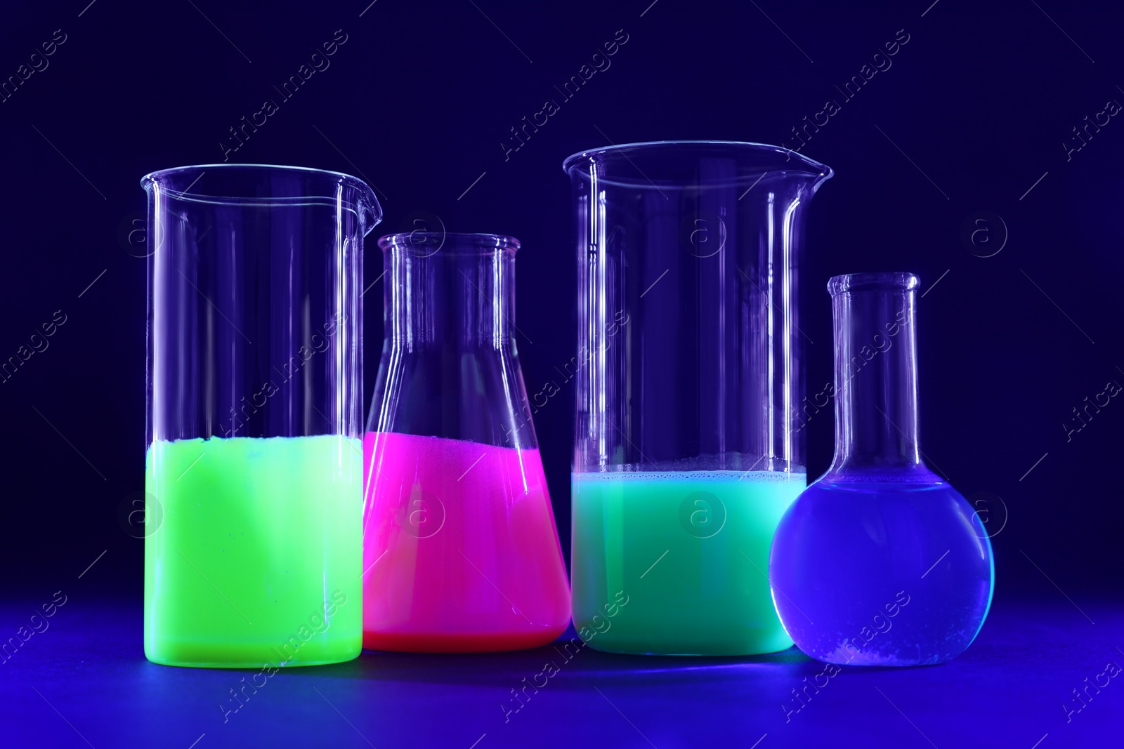 Photo of Laboratory glassware with luminous liquids on dark blue background