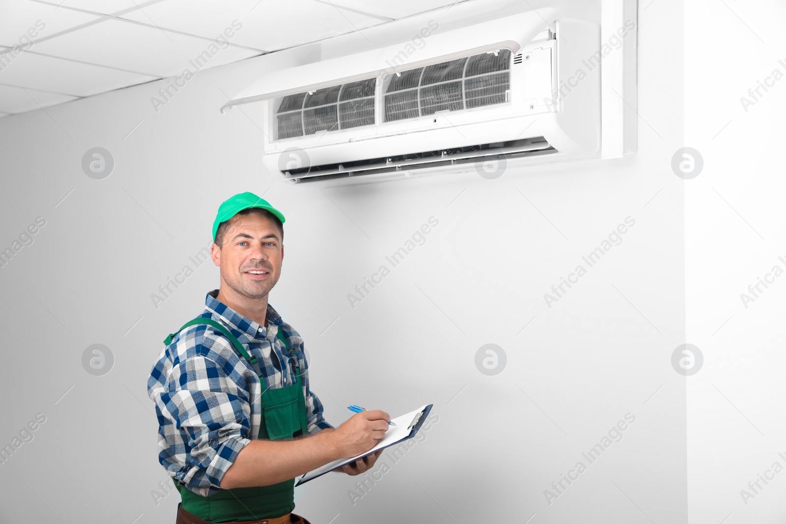 Photo of Technician with clipboard near air conditioner indoors