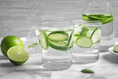 Photo of Glasses with fresh cucumber water on table against light background