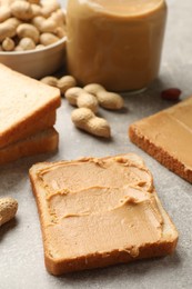 Photo of Tasty peanut butter sandwiches and peanuts on gray table, closeup