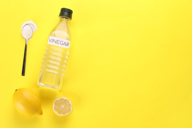 Photo of Eco friendly natural cleaners. Vinegar in bottle, lemons and spoon of soda on yellow background, flat lay. Space for text