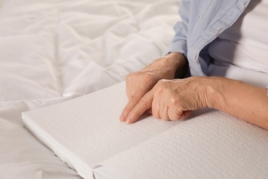 Blind senior person reading book written in Braille on bed, closeup