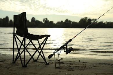 Folding chair and fishing rod on sand near river