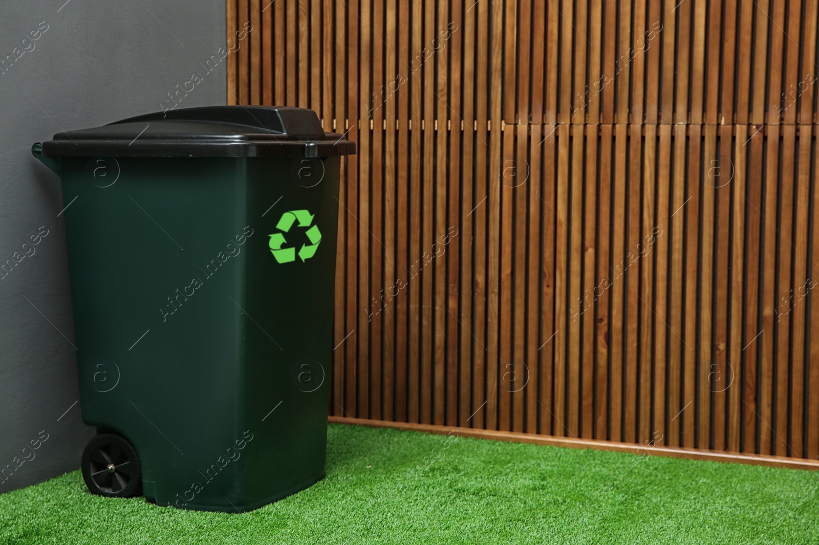 Photo of Trash bin with recycling symbol near wooden wall indoors. Space for text