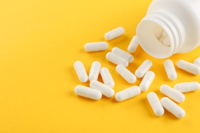 Photo of Bottle and vitamin capsules on yellow background, closeup. Space for text