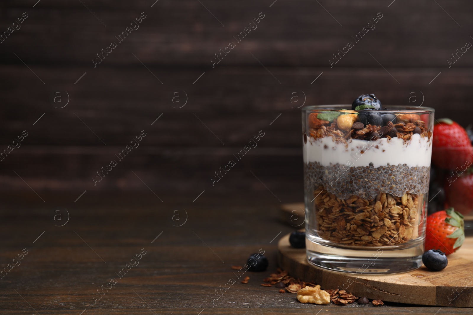 Photo of Tasty granola with berries, nuts, yogurt and chia seeds in glass on wooden table, space for text