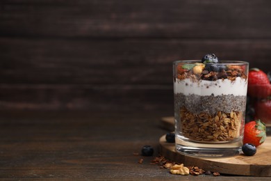 Photo of Tasty granola with berries, nuts, yogurt and chia seeds in glass on wooden table, space for text