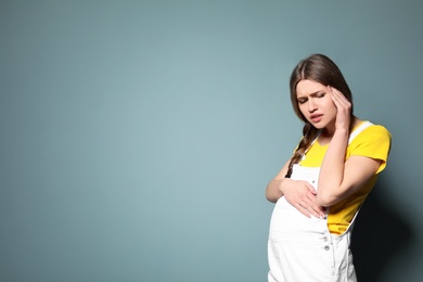 Photo of Young pregnant woman suffering from headache on color background