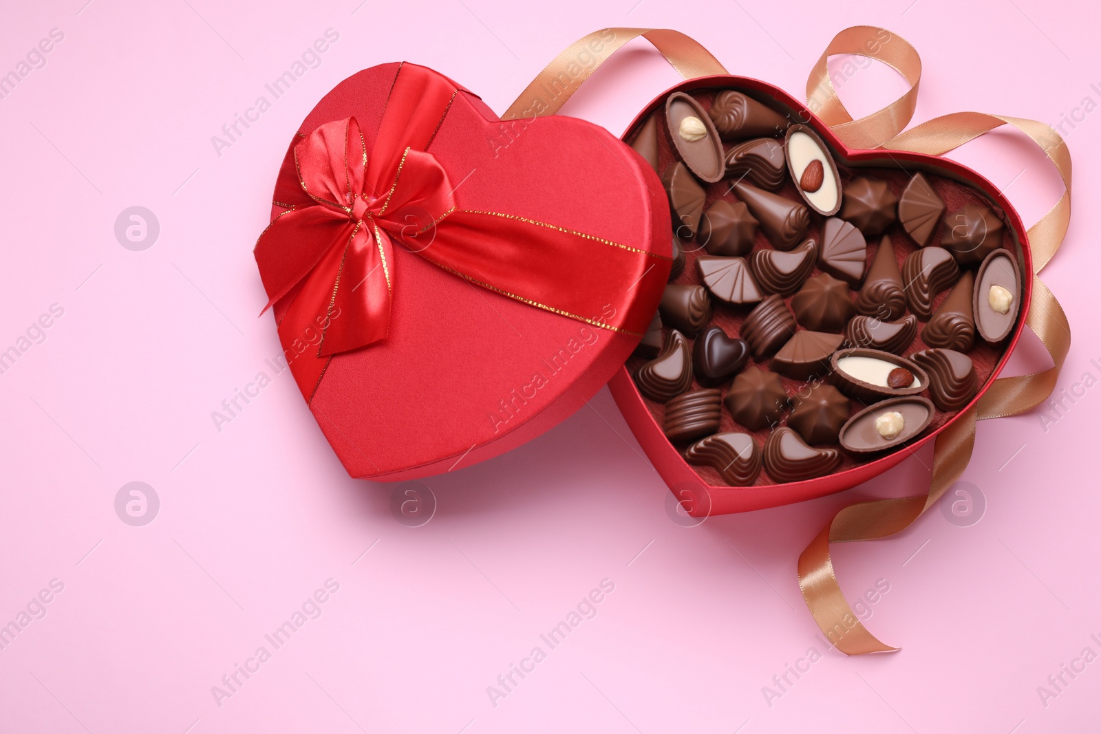 Photo of Heart shaped box with delicious chocolate candies and ribbon on pale pink background, flat lay. Space for text