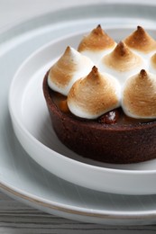 Photo of Delicious salted caramel chocolate tart with meringue on white table, closeup