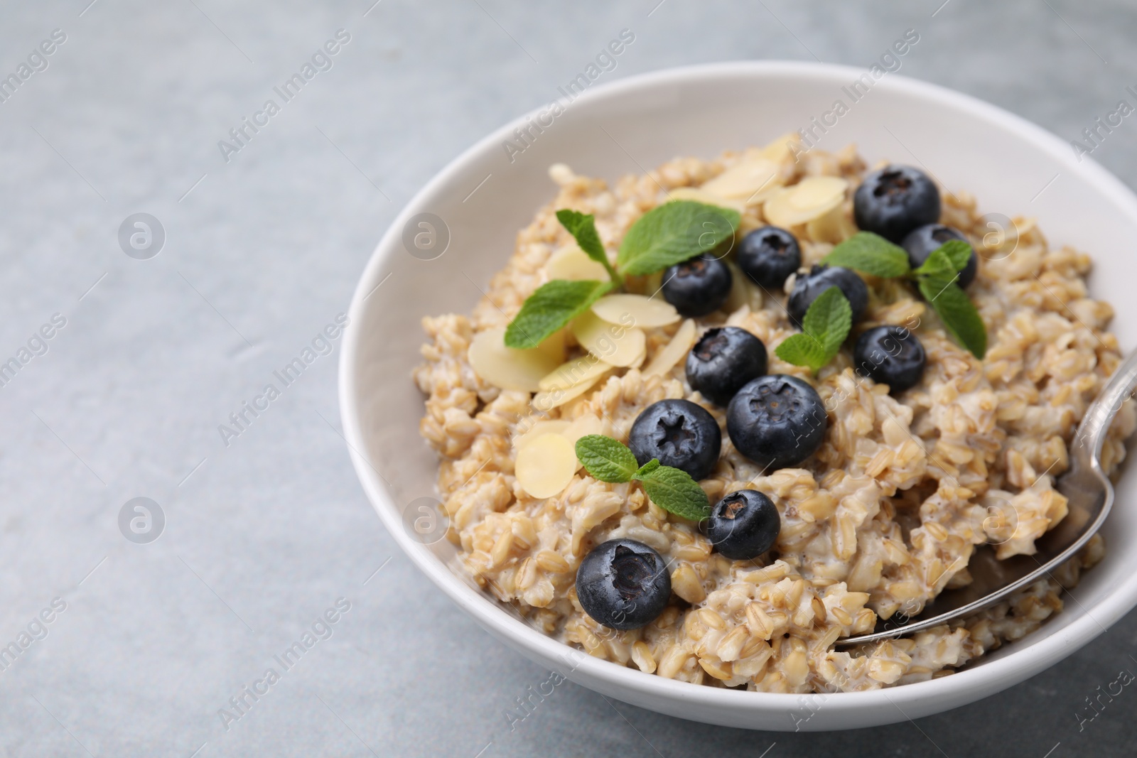 Photo of Tasty oatmeal with blueberries, mint and almond petals in bowl on grey table, closeup. Space for text