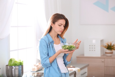 Sad young woman eating salad in kitchen. Healthy diet