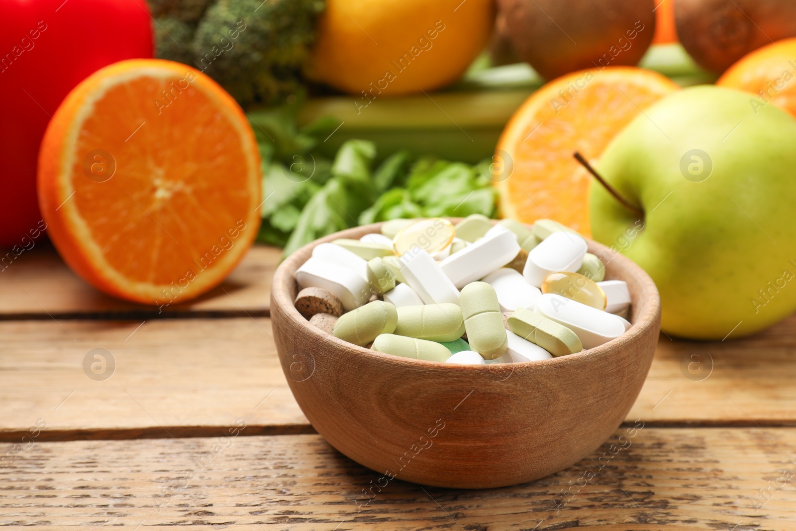 Photo of Dietary supplements. Different pills in bowl and food products on wooden table, closeup