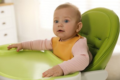 Photo of Cute little baby wearing bib in highchair indoors