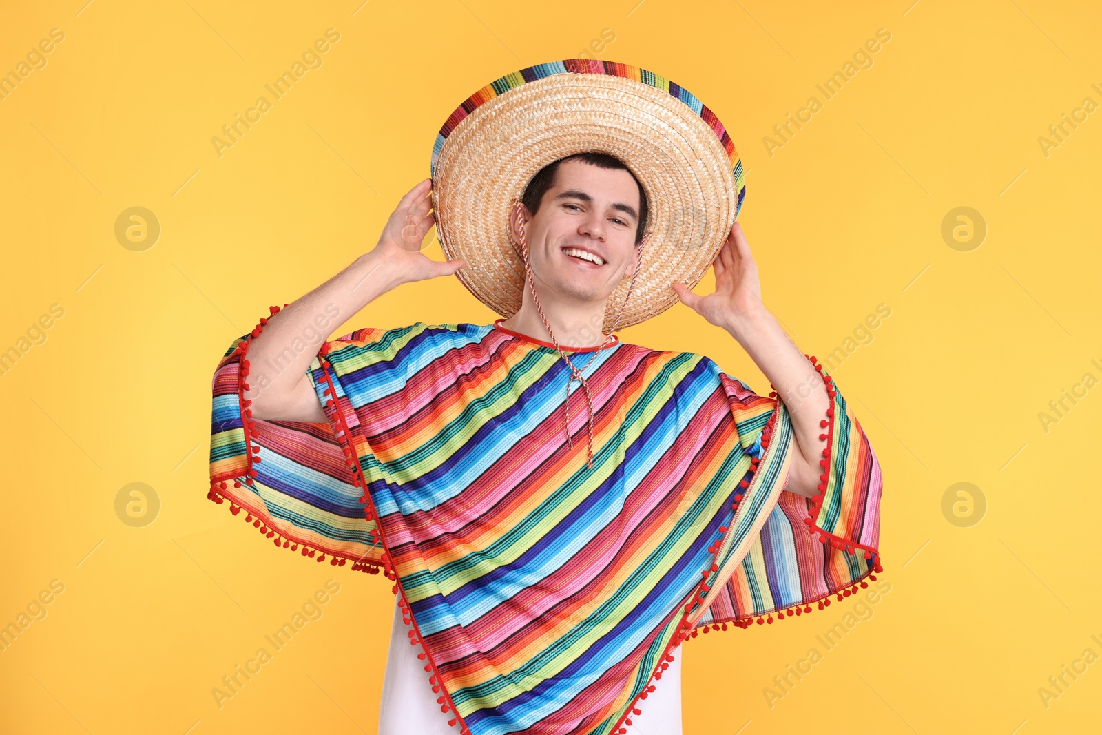 Photo of Young man in Mexican sombrero hat and poncho on yellow background