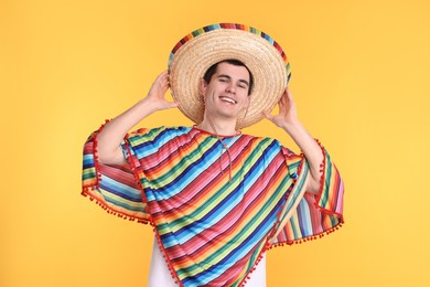 Photo of Young man in Mexican sombrero hat and poncho on yellow background