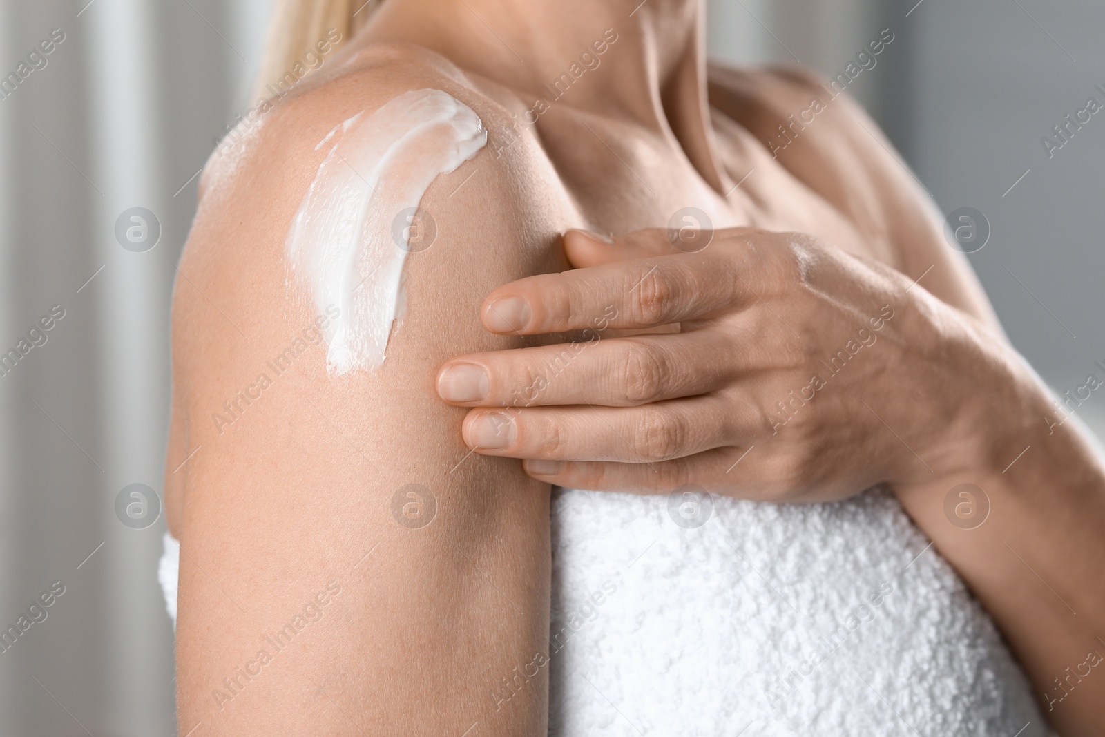 Photo of Woman applying body cream onto shoulder indoors, closeup