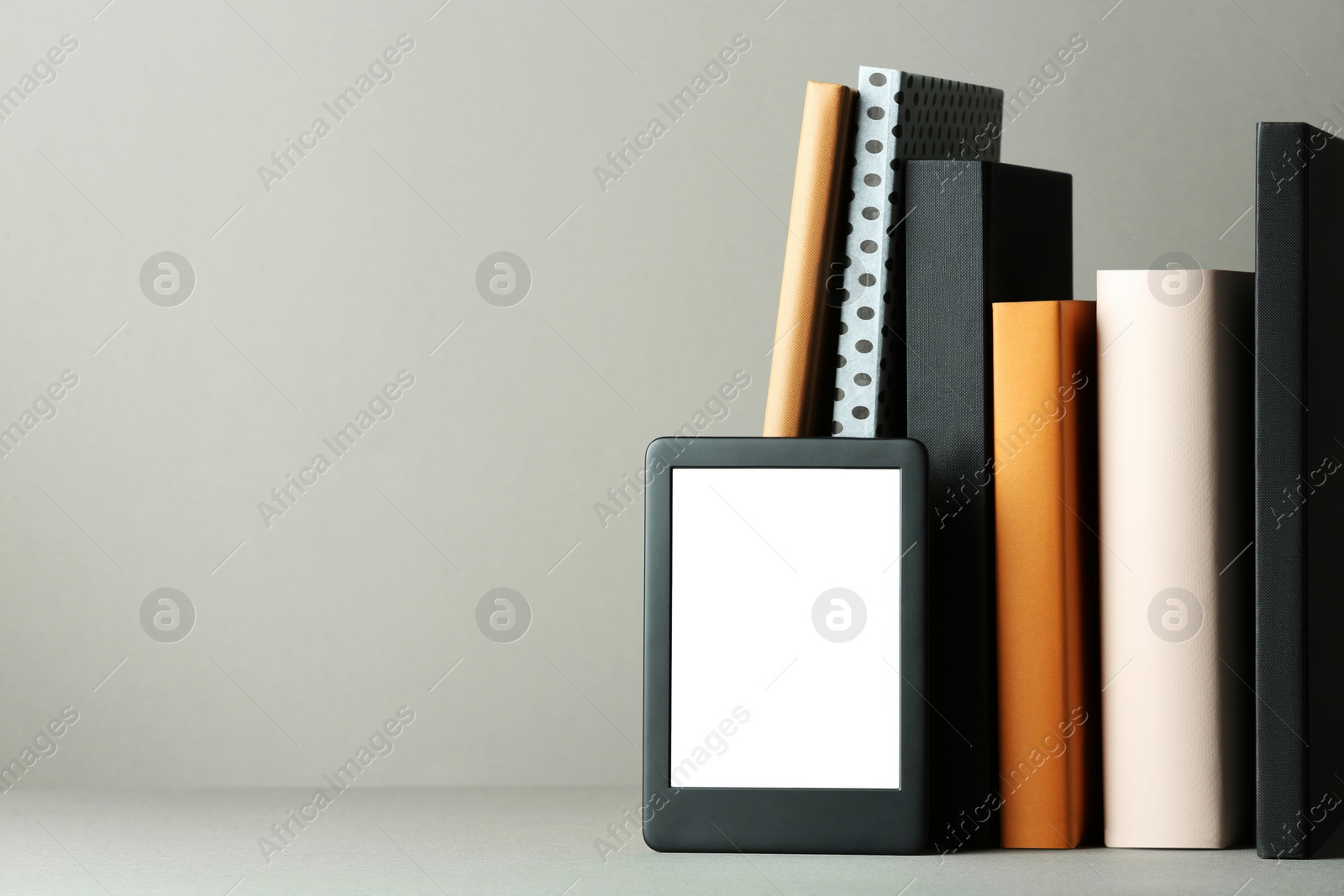 Photo of Modern e-book reader and hard cover books on light grey table. Space for text
