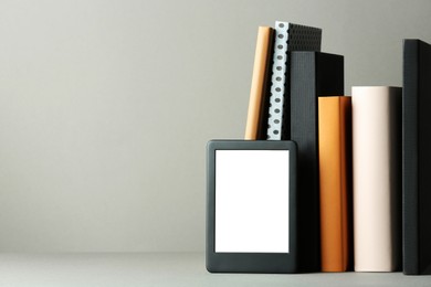Modern e-book reader and hard cover books on light grey table. Space for text