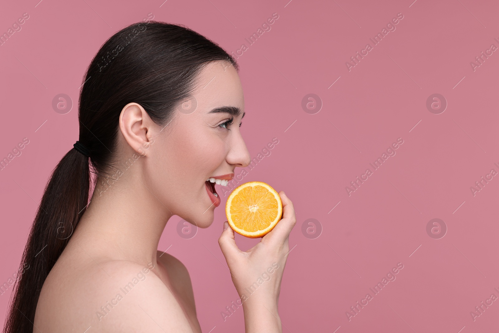 Photo of Beautiful young woman with piece of orange on pink background. Space for text