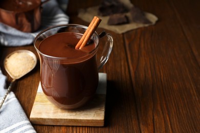 Cup of delicious hot chocolate with cinnamon stick on wooden table, space for text