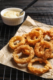 Photo of Cooling rack with homemade crunchy fried onion rings and sauce on wooden background