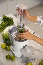 Young woman making tasty fresh juice at table in kitchen, closeup