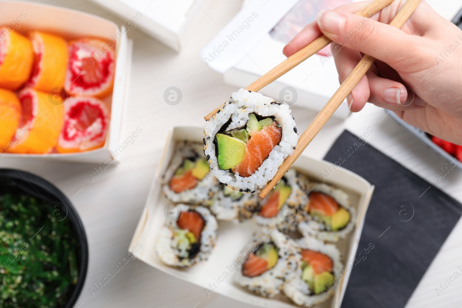 Photo of Woman eating sushi rolls with chopsticks at white table, top view