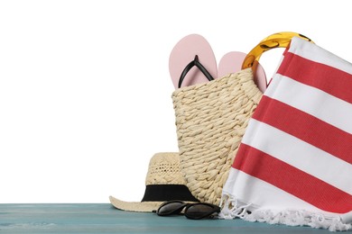 Beach bag with towel, flip flops, hat and sunglasses on light blue wooden surface against white background. Space for text