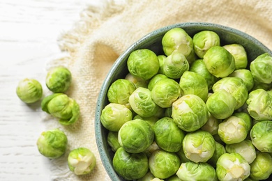 Photo of Bowl of fresh Brussels sprouts and napkin on wooden background, top view