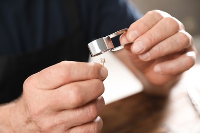 Male jeweler evaluating earring at table in workshop, closeup