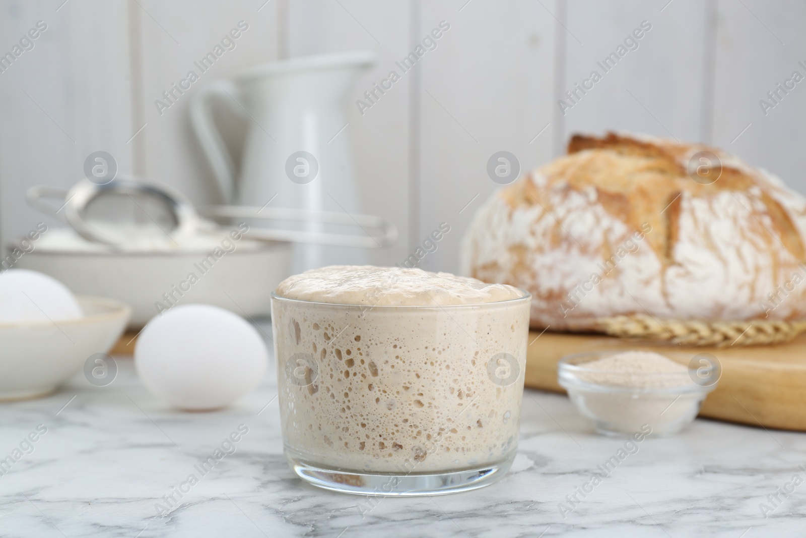 Photo of Glass jar with sourdough on white marble table