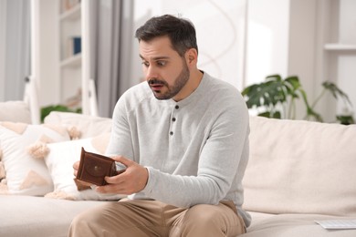 Photo of Confused man with empty wallet at home. Debt problem