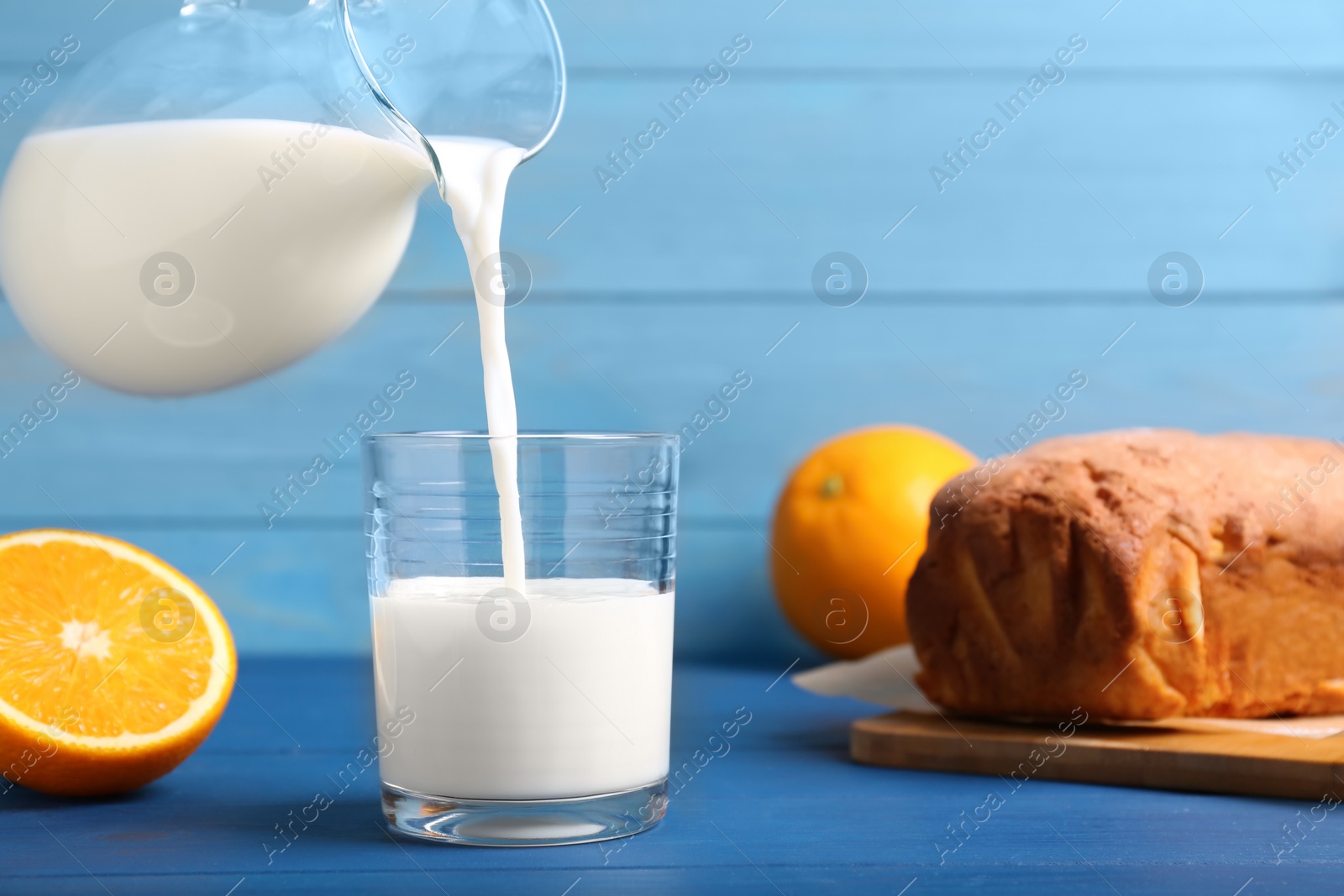 Photo of Pouring milk into glass and fresh cake on blue wooden table