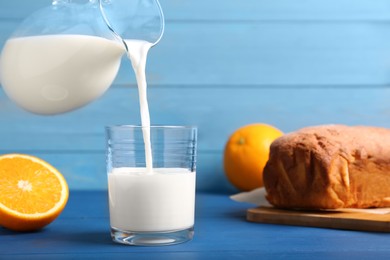 Photo of Pouring milk into glass and fresh cake on blue wooden table