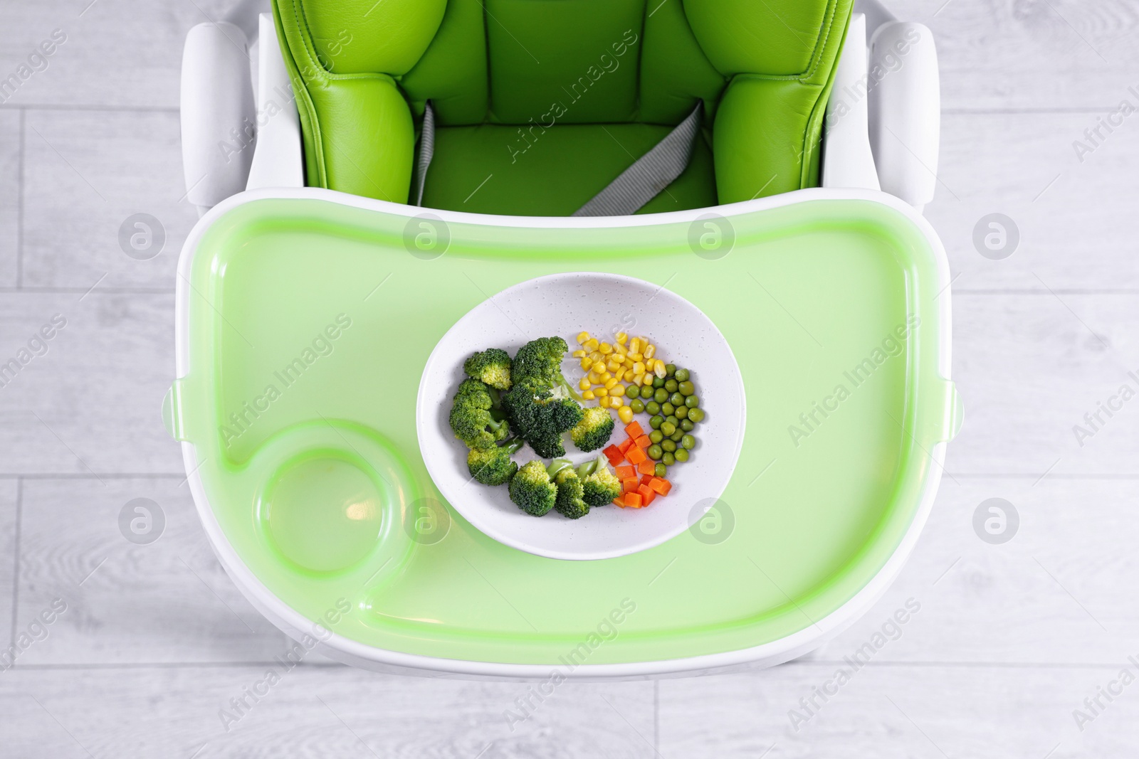 Photo of High chair with healthy baby food served on light green tray indoors, top view