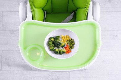 Photo of High chair with healthy baby food served on light green tray indoors, top view