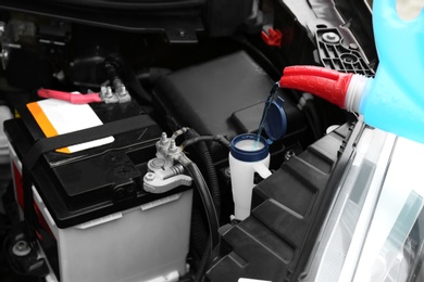 Pouring liquid from plastic canister into car washer fluid reservoir, closeup