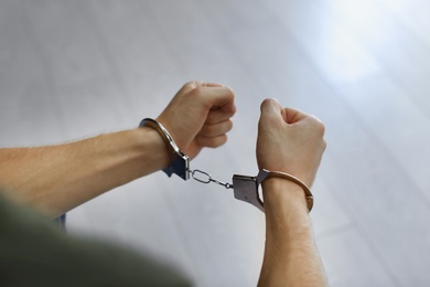 Man detained in handcuffs indoors, closeup view. Criminal law