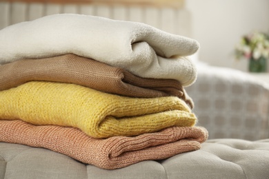 Photo of Stack of stylish knitted sweaters in bedroom, closeup