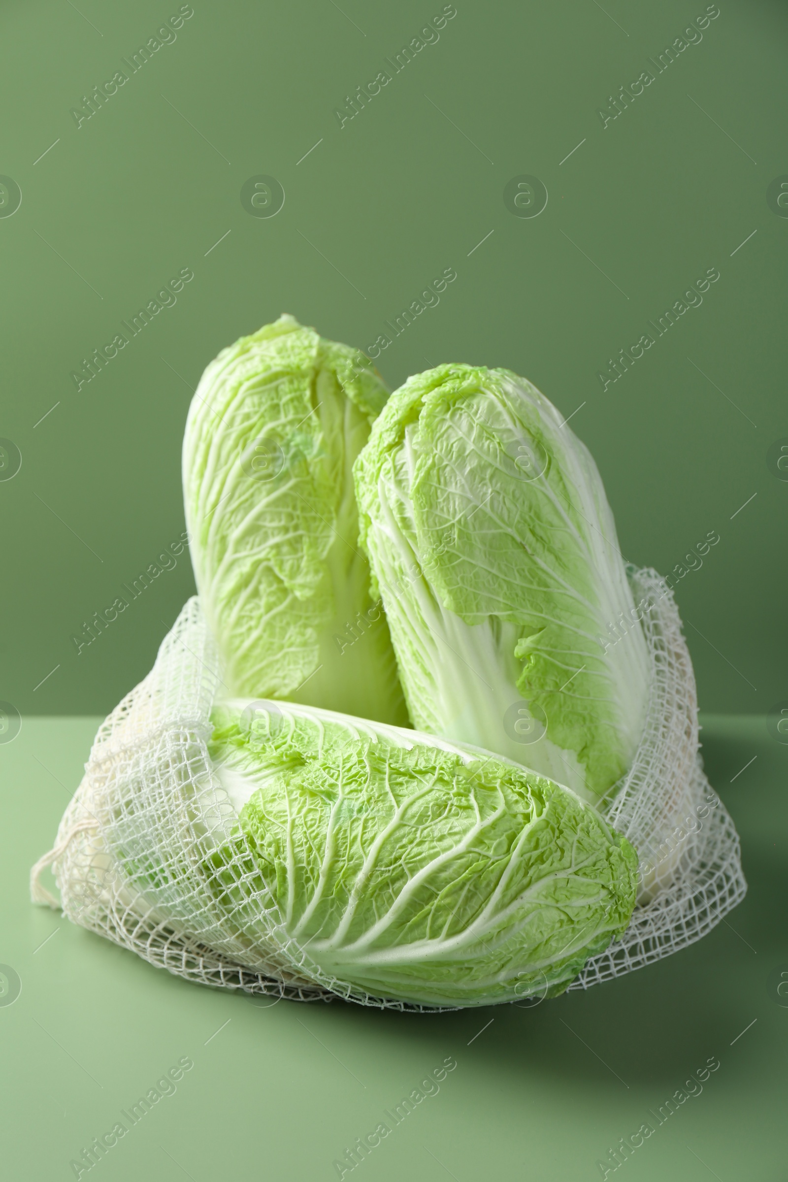 Photo of Fresh Chinese cabbages in string bag on green background