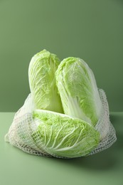 Photo of Fresh Chinese cabbages in string bag on green background