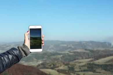 Woman taking photo of beautiful mountain landscape with smartphone