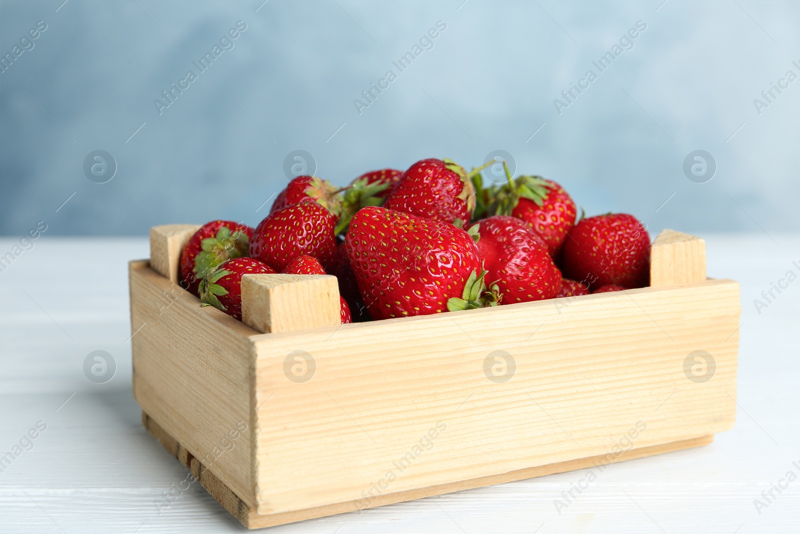 Photo of Delicious ripe strawberries in crate on white wooden table