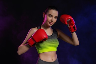 Photo of Portrait of beautiful woman wearing boxing gloves in color lights on black background