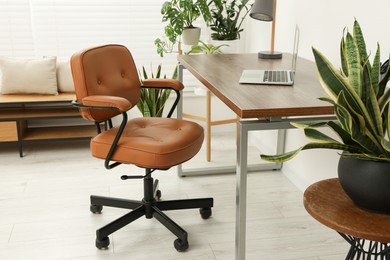 Photo of Stylish office interior with comfortable chair, desk, laptop and houseplants