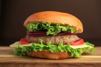 Tasty burger with vegetables, patty and cheese on wooden table, closeup